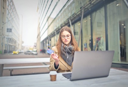 A woman holding a payment card while using a laptop outdoors