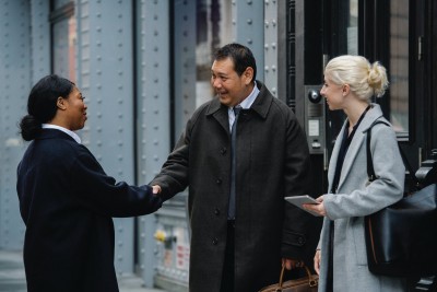 Three businesspeople meeting outside an office building, two shaking hands